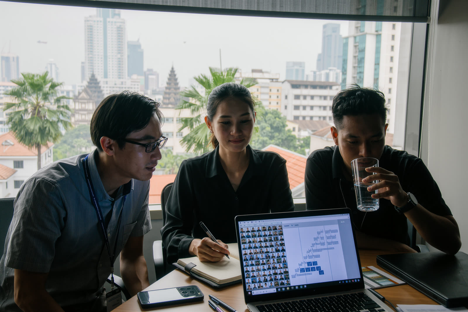 A team of mid-level professionals in Phnom Penh, Cambodia joining a live online-led Lean Six Sigma training session together around a laptop.